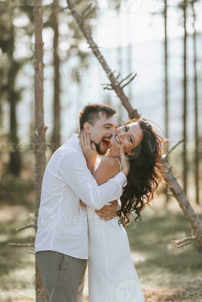 stilvoll Bräutigam im Weiß Hemd und süß Brünette Braut im Weiß Kleid im Wald in der Nähe von Hochzeit hölzern Bogen. Hochzeit Porträt von Jungvermählten. foto