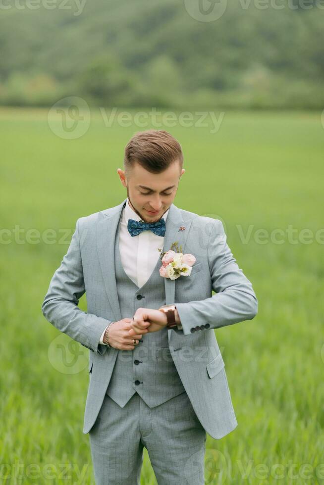 Porträt von ein Bräutigam Stehen auf das Hintergrund von ein Grün Feld, suchen beim seine betrachten. stilvoll Bräutigam. Mode und Stil. foto