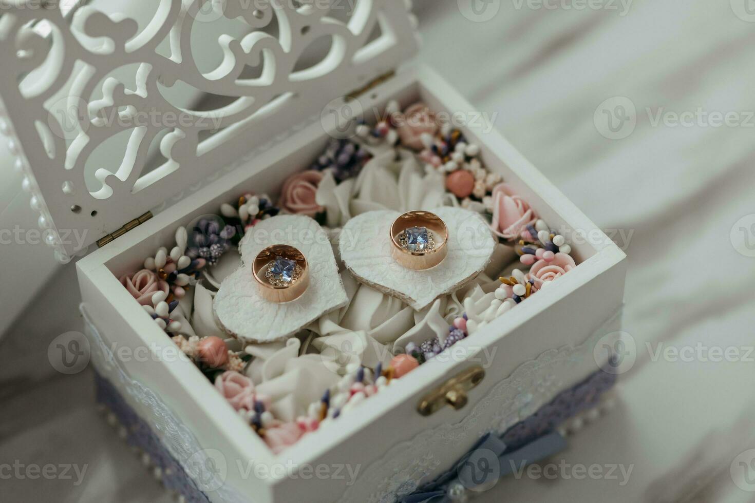 Hochzeit Ringe im ein hölzern Box Stand auf ein herzförmig Stand gefüllt mit Blumen auf ein Weiß Hintergrund. Hochzeit Einzelheiten. foto