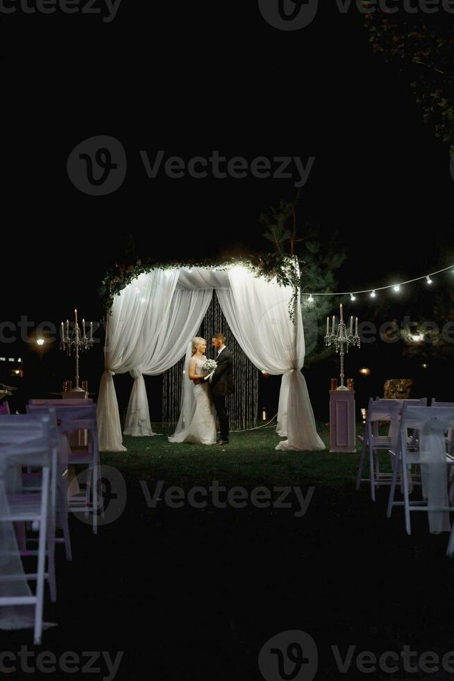 Hochzeit Zeremonie auf das Ufer von das See. Gemälde Zeremonie im das Abend. romantisch malen. das Präsidium ist dekoriert mit Weiß Blumen. Weiß Stühle. das Braut und Bräutigam sanft halt Hände foto