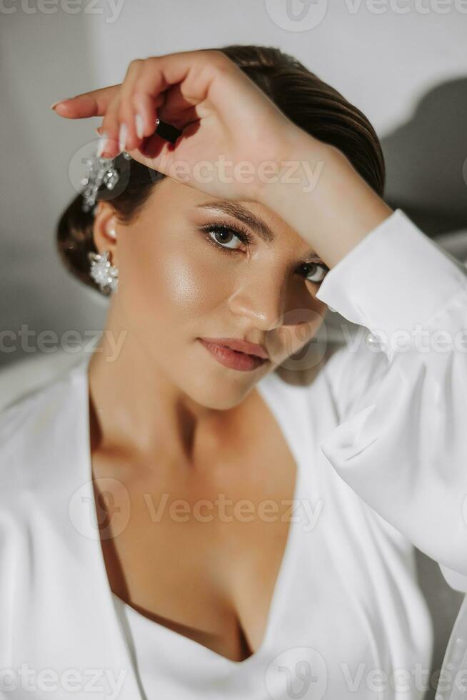 ein jung Braut im ein Weiß Kleid ist Lügen auf das Kante von das Sofa, Porträt Foto. Vorbereitung zum das Hochzeit Zeremonie. Zubehör zum Jungvermählten foto