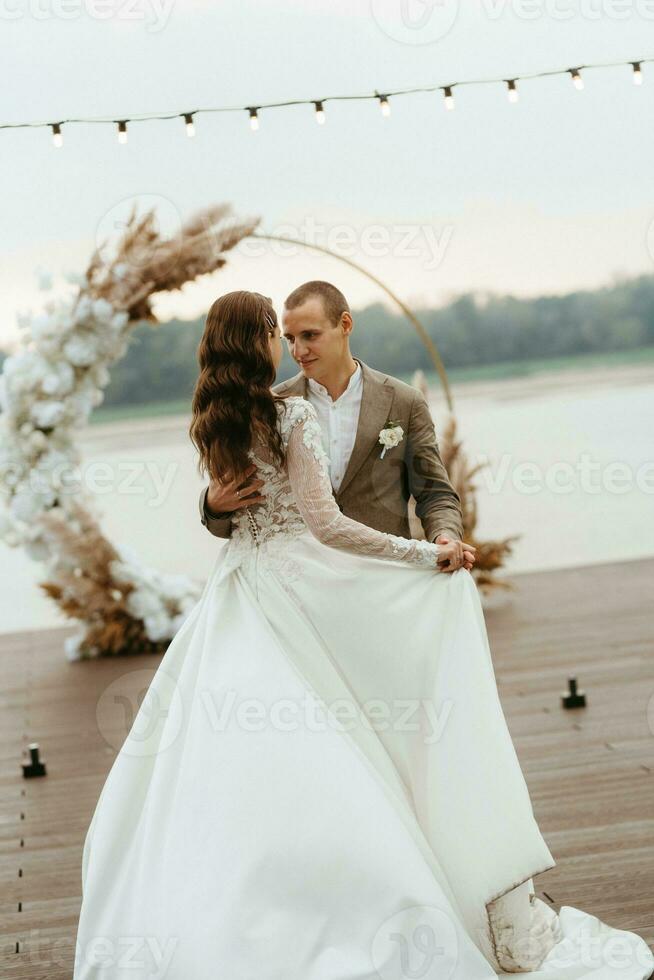 das zuerst Hochzeit tanzen von das Braut und Bräutigam auf das Seebrücke in der Nähe von das Fluss foto