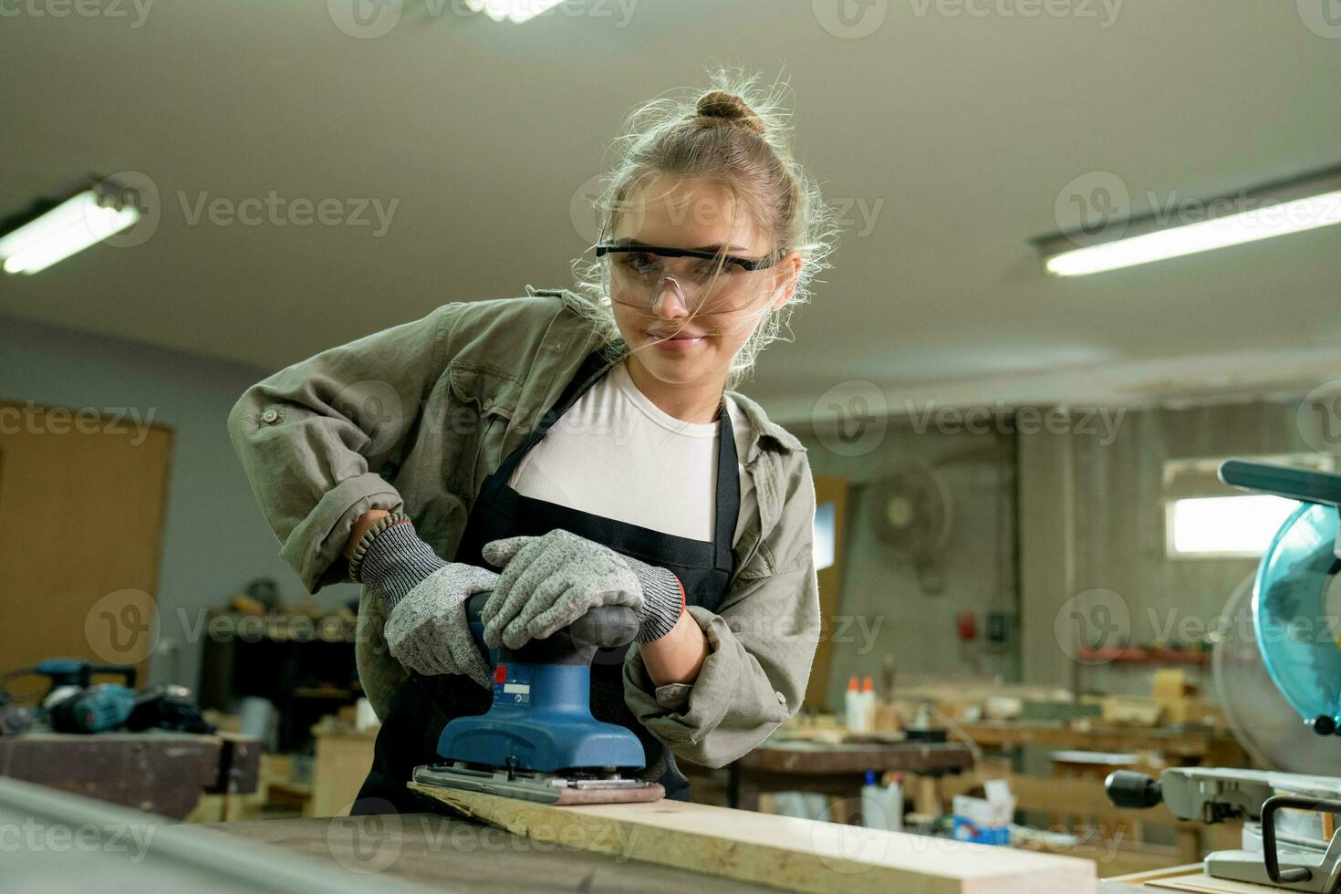 weiblich Zimmermann tragen schützend Sicherheit Brille und mit elektrisch Arbeit auf ein Holz. Künstler oder Möbel Designer Arbeiten auf ein Produkt Idee im ein Werkstatt. foto