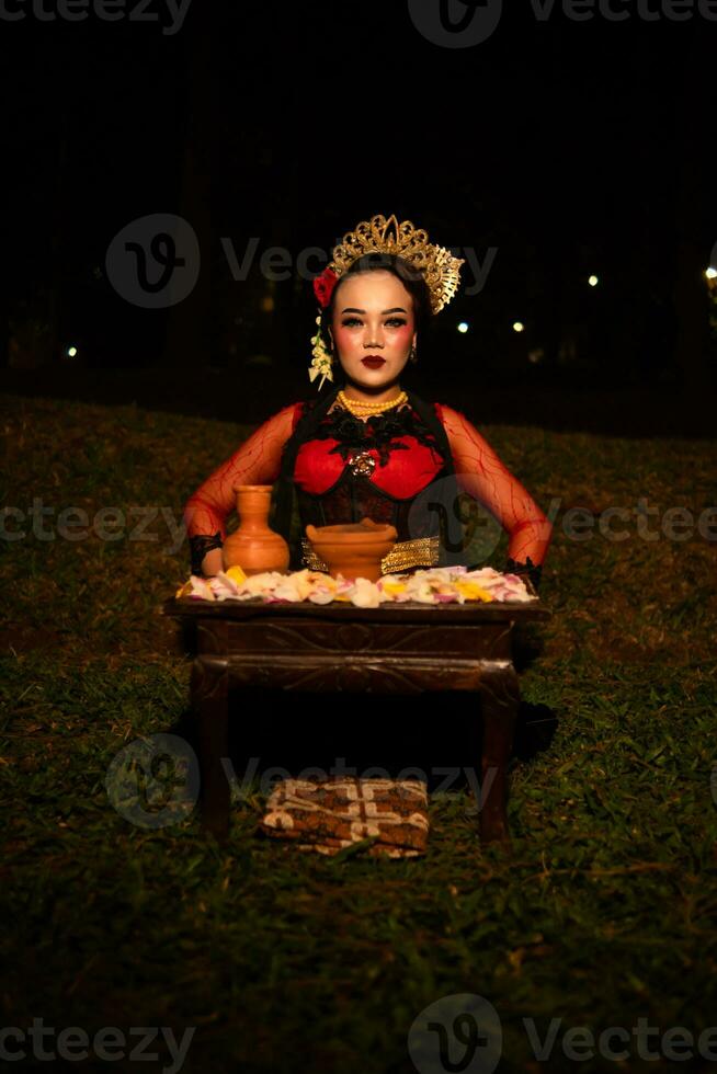 breit Schuss von ein asiatisch Mädchen im traditionell Kleider Sitzung im ein Wald mit ein Tabelle voll von Blumen foto