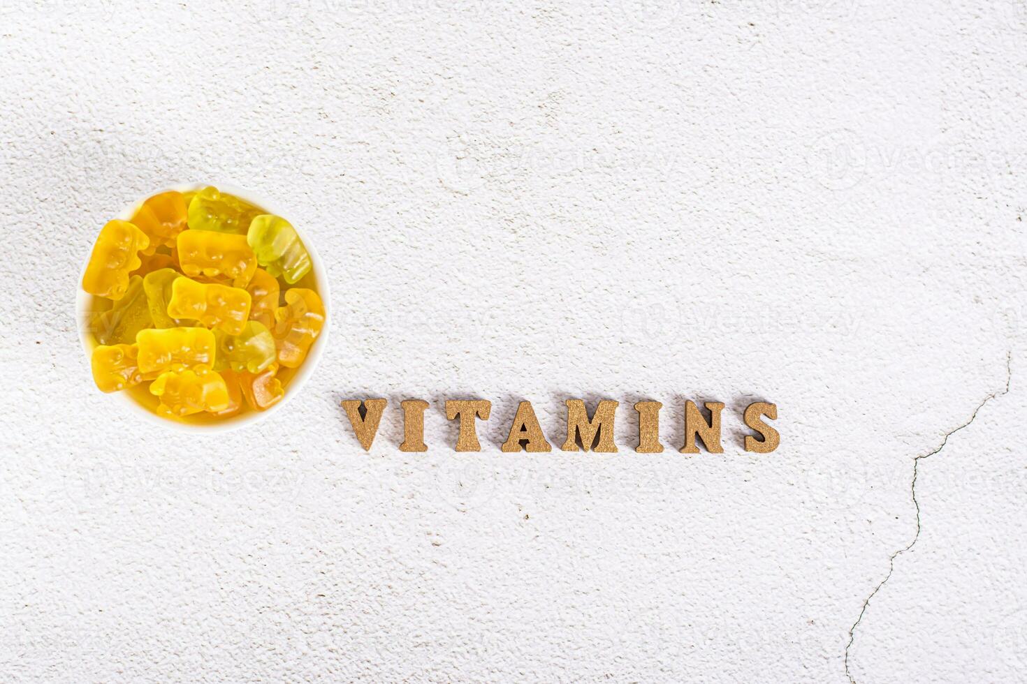 das Wort Vitamine von Briefe und kaubar Vitamine im das bilden von Süßigkeiten Bären im ein Schüssel oben Aussicht foto