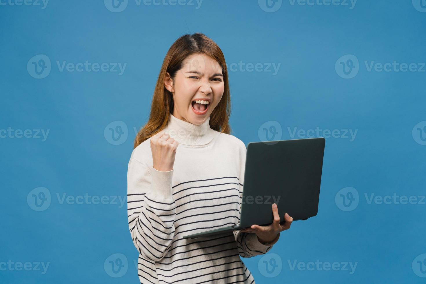 junge asiatische Dame mit Laptop mit positivem Ausdruck, lächelt breit, in Freizeitkleidung gekleidet, fühlt sich glücklich und steht isoliert auf blauem Hintergrund. glückliche entzückende frohe frau freut sich über erfolg. foto