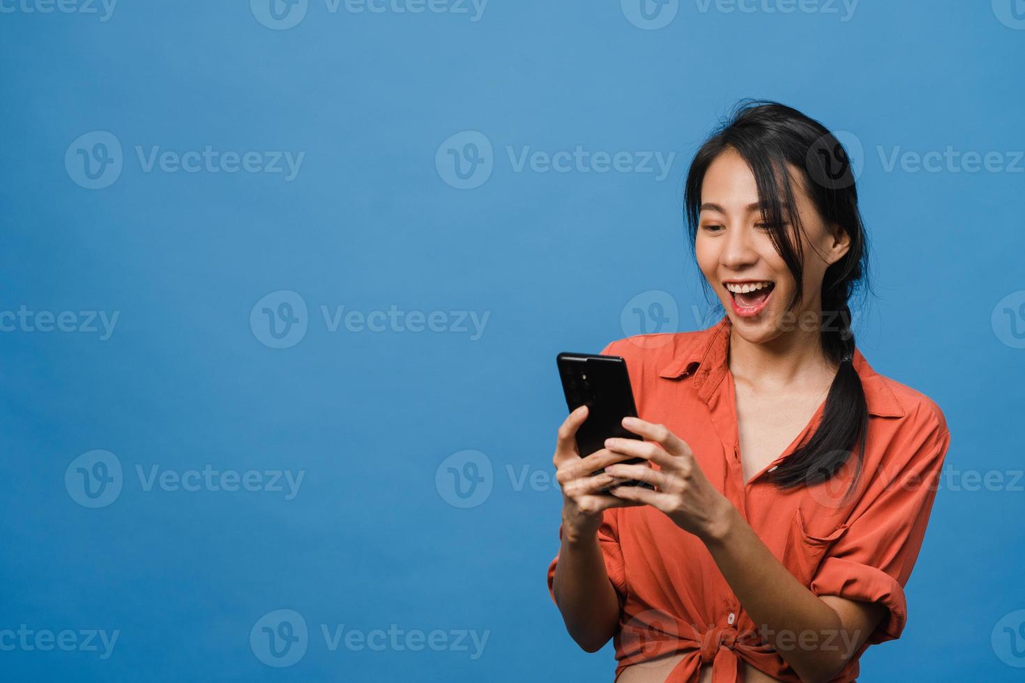 junge asiatische dame, die telefon mit positivem ausdruck verwendet, breit lächelt, in lässiger kleidung gekleidet fühlt sich glücklich und steht einzeln auf blauem hintergrund. glückliche entzückende frohe frau freut sich über erfolg. foto