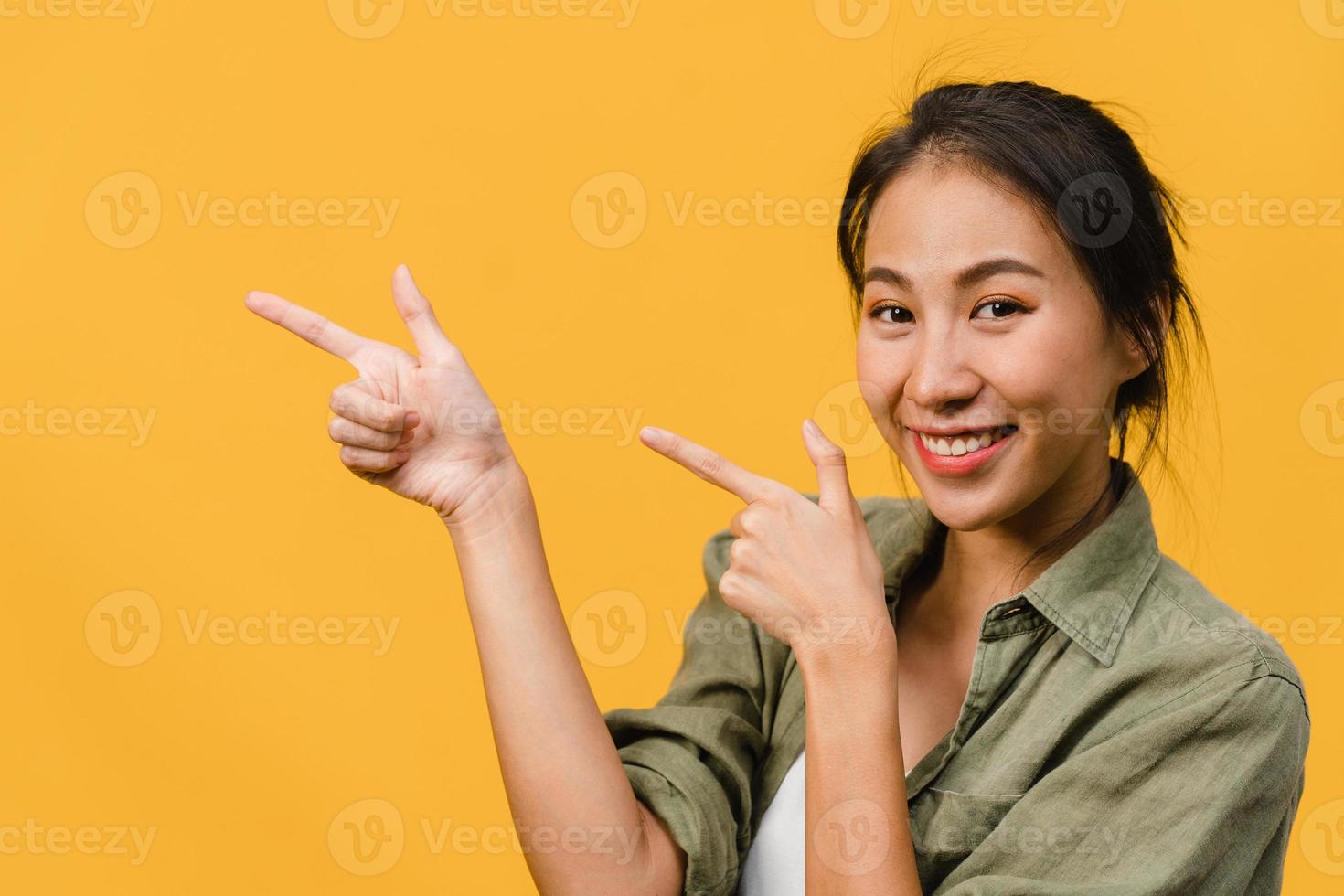 Porträt einer jungen asiatischen Dame, die mit fröhlichem Ausdruck lächelt, zeigt etwas Erstaunliches an leeren Stellen in legerem Tuch und blickt auf die Kamera einzeln auf gelbem Hintergrund. Gesichtsausdruck Konzept. foto