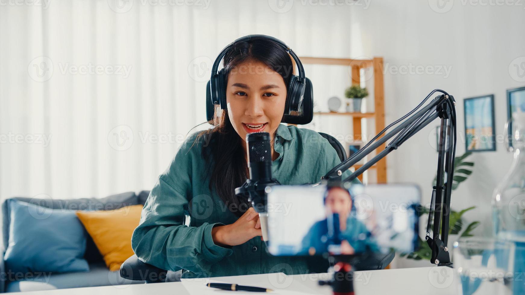 Teenager Asia Girl Influencer verwenden Mikrofon tragen Kopfhörer Aufnahmeinhalte mit Smartphone für Online-Publikum zu Hause hören. Studentische Podcasterin macht Audio-Podcast aus ihrem Heimstudio. foto