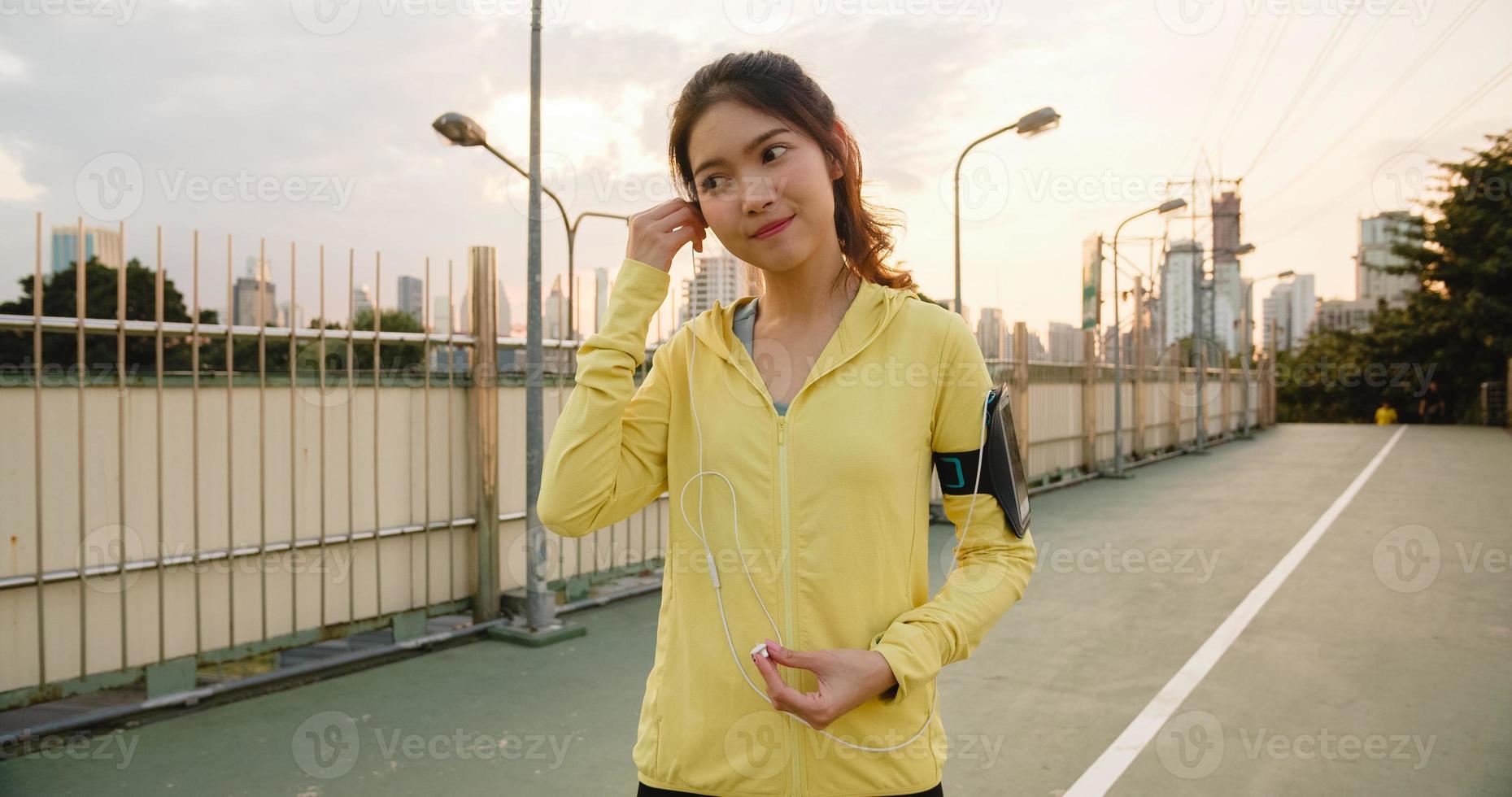 Schöne junge asiatische Sportlerin trainiert mit dem Smartphone, um Musik beim Laufen in der städtischen Umgebung zu hören. koreanisches jugendlich Mädchen, das am frühen Morgen Sportkleidung auf der Gehwegbrücke trägt. foto