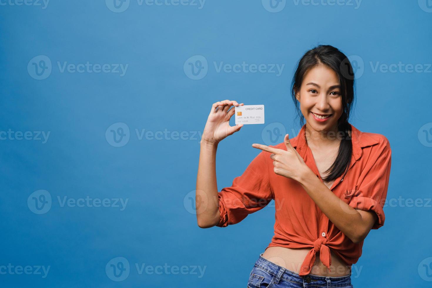 junge asiatische Dame zeigt Kreditkarte mit positivem Ausdruck, lächelt breit, in Freizeitkleidung gekleidet, fühlt sich glücklich und steht einzeln auf blauem Hintergrund. Gesichtsausdruck Konzept. foto