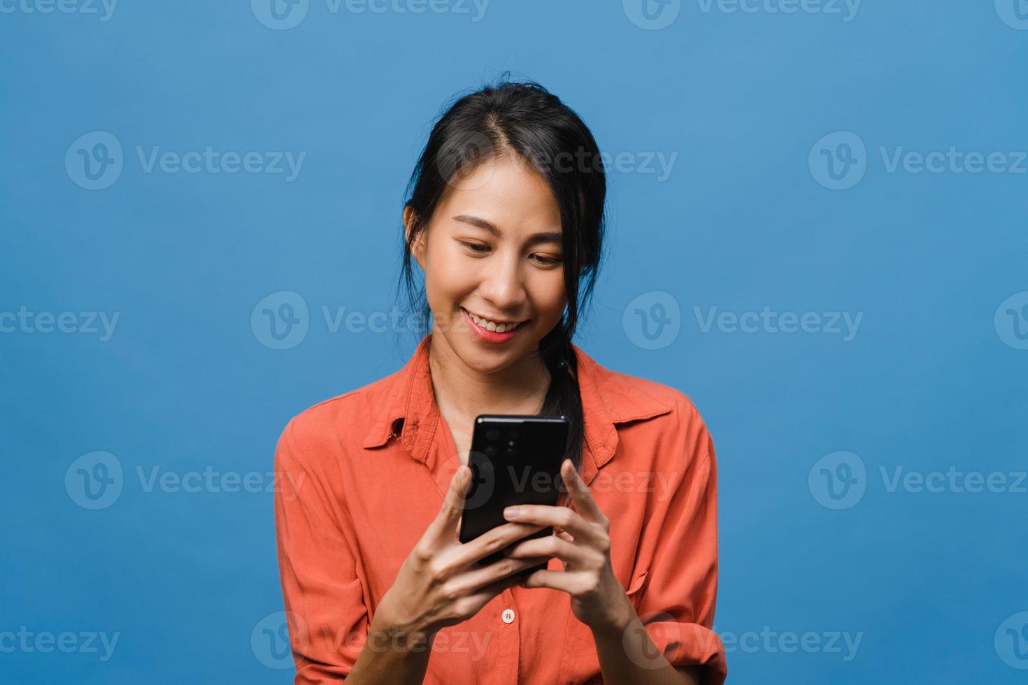 junge asiatische dame, die telefon mit positivem ausdruck verwendet, breit lächelt, in lässiger kleidung gekleidet fühlt sich glücklich und steht einzeln auf blauem hintergrund. glückliche entzückende frohe frau freut sich über erfolg. foto