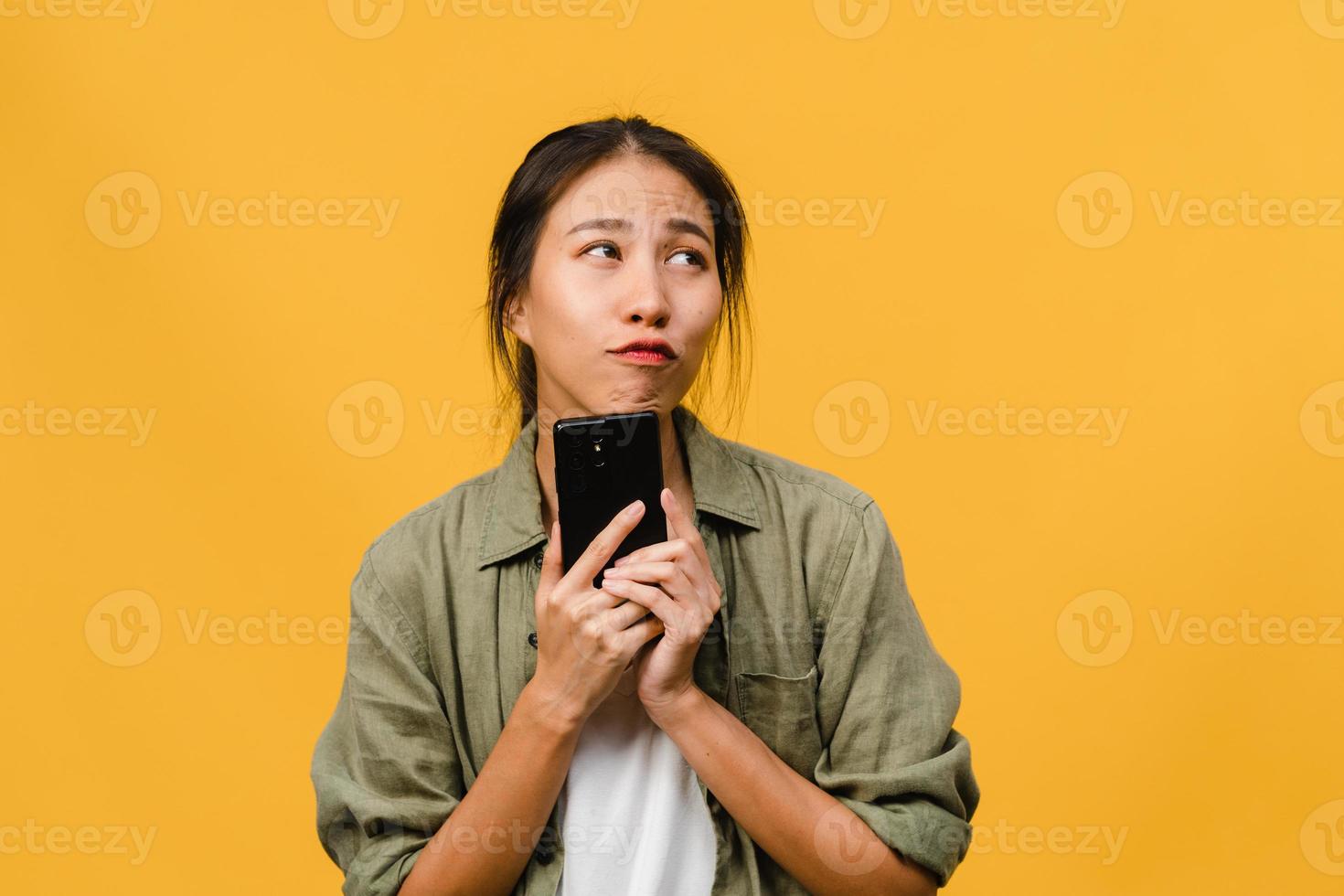 junge asiatische dame, die telefon mit positivem ausdruck verwendet, breit lächelt, in lässiger kleidung gekleidet fühlt sich glücklich und steht einzeln auf gelbem hintergrund. glückliche entzückende frohe frau freut sich über erfolg. foto