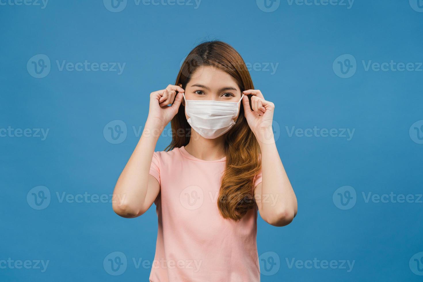 Junges asiatisches Mädchen, das eine medizinische Gesichtsmaske trägt, in Freizeitkleidung gekleidet ist und die Kamera einzeln auf blauem Hintergrund betrachtet. Selbstisolation, soziale Distanzierung, Quarantäne zur Vorbeugung des Coronavirus. foto