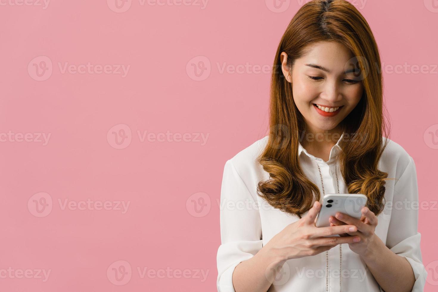junge asiatische dame, die telefon mit positivem ausdruck benutzt, breit lächelt, in lässiger kleidung gekleidet, glücklich fühlt und isoliert auf rosa hintergrund steht. glückliche entzückende frohe frau freut sich über erfolg. foto