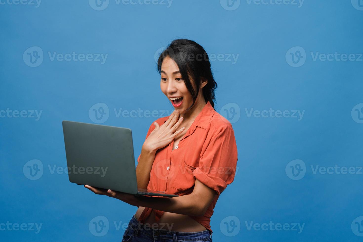 junge asiatische Dame mit Laptop mit positivem Ausdruck, lächelt breit, in Freizeitkleidung gekleidet, fühlt sich glücklich und steht isoliert auf blauem Hintergrund. glückliche entzückende frohe frau freut sich über erfolg. foto