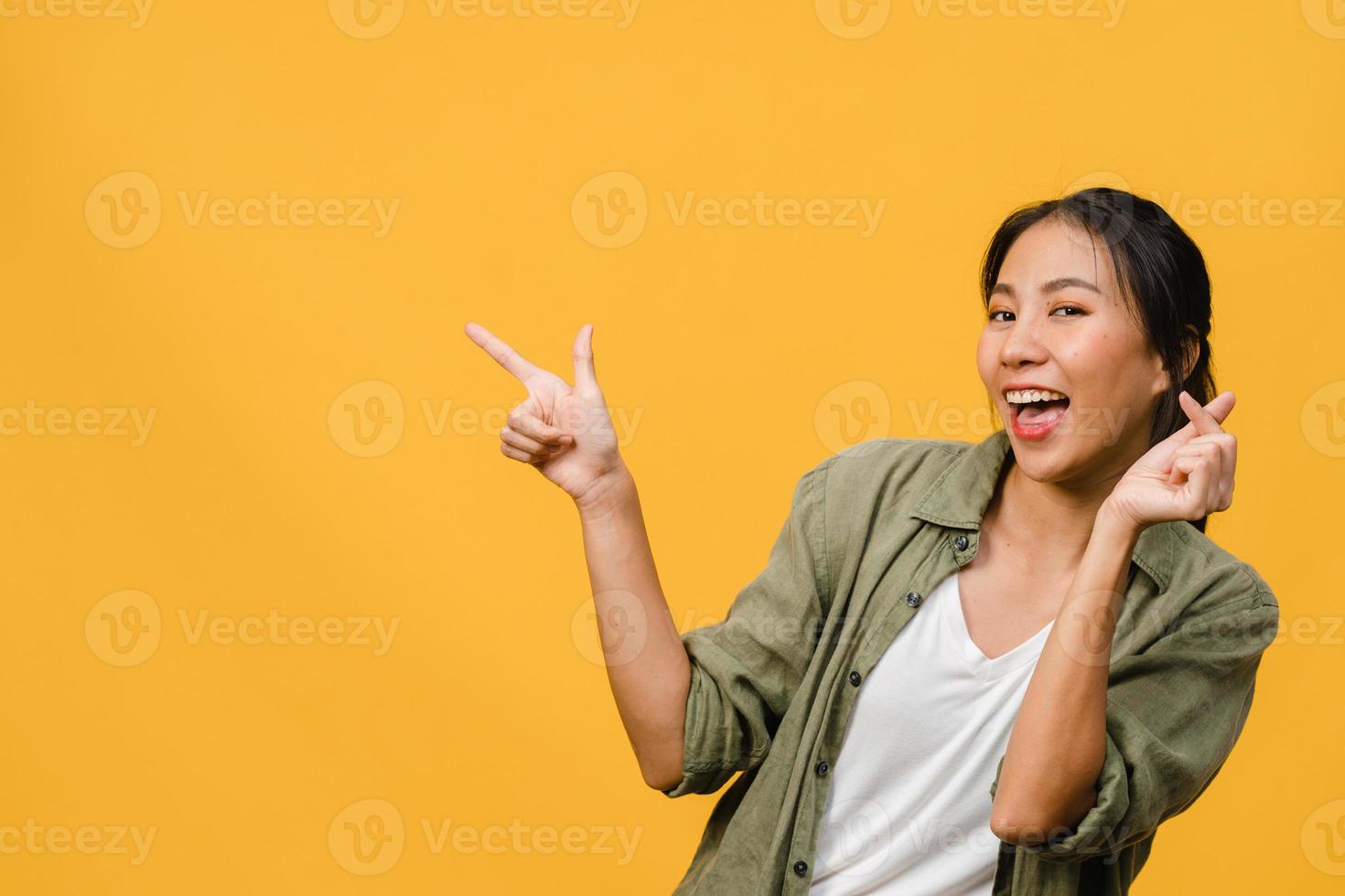 Porträt einer jungen asiatischen Dame, die mit fröhlichem Ausdruck lächelt, zeigt etwas Erstaunliches an leeren Stellen in legerem Tuch und blickt auf die Kamera einzeln auf gelbem Hintergrund. Gesichtsausdruck Konzept. foto