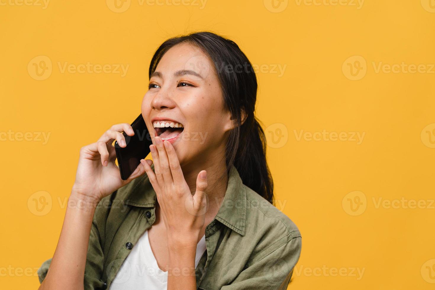 junge asiatische Dame telefoniert mit positivem Ausdruck, lächelt breit, in Freizeitkleidung gekleidet, fühlt sich glücklich und steht isoliert auf gelbem Hintergrund. glückliche entzückende frohe frau freut sich über erfolg. foto