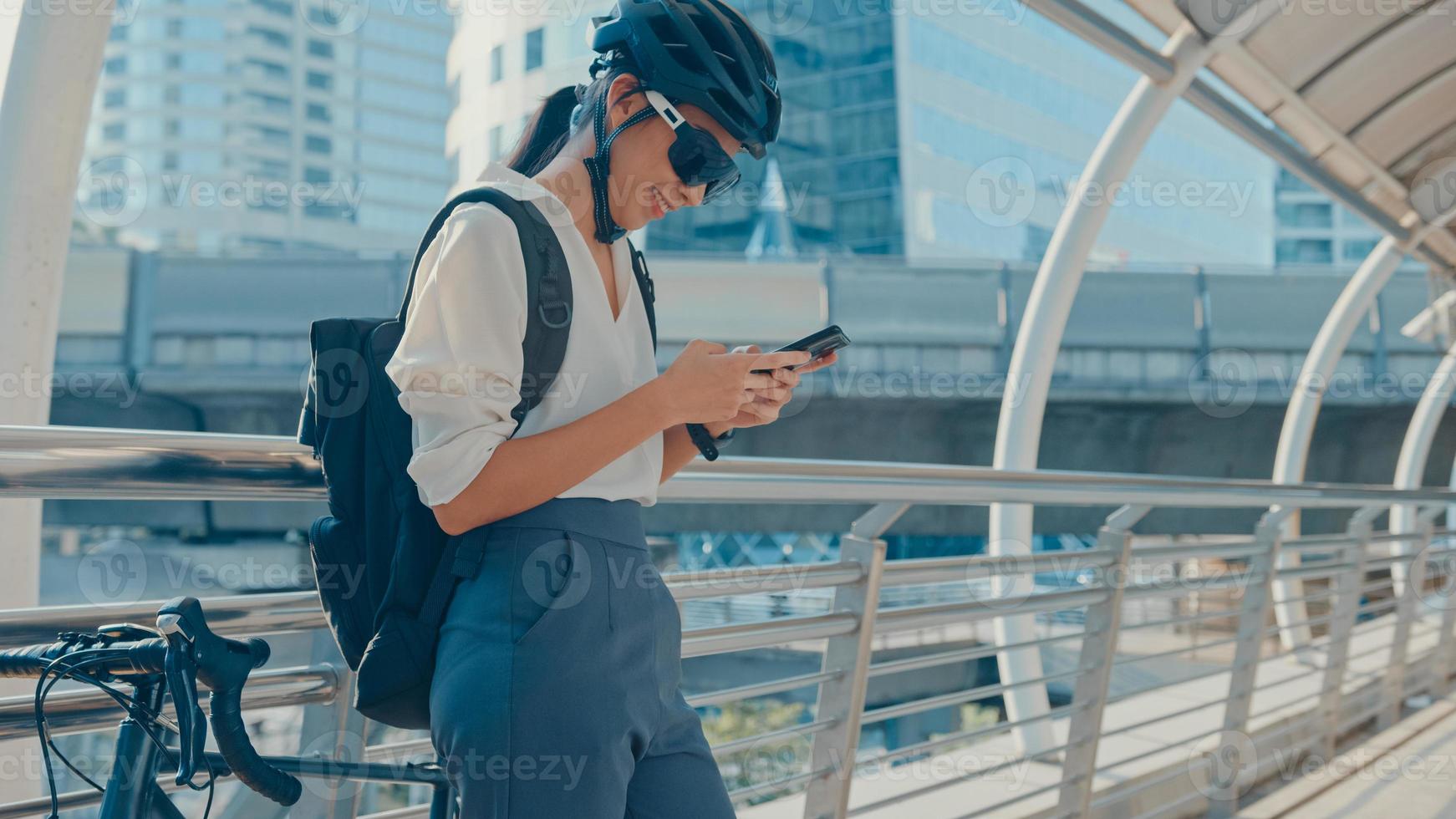 glückliche asiatische geschäftsfrau mit rucksack nutzt Smartphone im stadtstand an der straße mit fahrrad zur arbeit im büro. Sportmädchen benutzen ihr Telefon für den Arbeitsjob. zur Arbeit pendeln, Berufspendler in der Stadt. foto