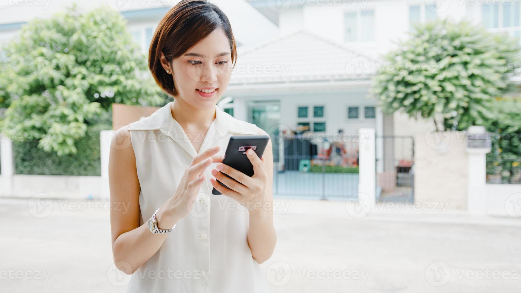 Attraktive junge Geschäftsfrau in Asien, die mit dem Handy das Internet in sozialen Medien überprüft und mit Freunden draußen auf der Straße in der Stadt chattet. Lebensstil nach Coronavirus und sozialer Distanzierung neu normal. foto