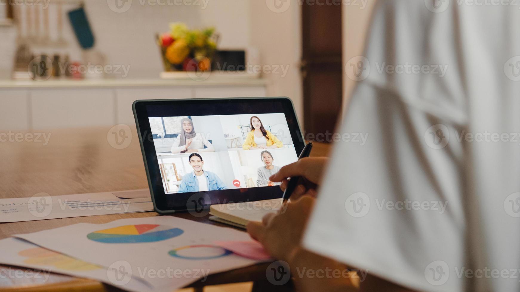 Asiatische Geschäftsfrau, die ein digitales Tablet verwendet, spricht mit einem Kollegen über den Plan per Videoanruf, Brainstorming-Online-Meeting, während sie von zu Hause aus in der Küche arbeitet. soziale Distanzierung, Quarantäne wegen Corona-Virus. foto