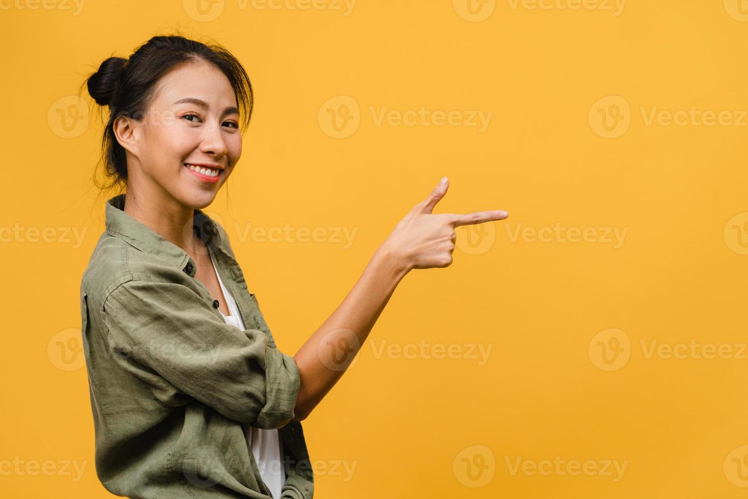 Porträt einer jungen asiatischen Dame, die mit fröhlichem Ausdruck lächelt, zeigt etwas Erstaunliches an leeren Stellen in legerem Tuch und blickt auf die Kamera einzeln auf gelbem Hintergrund. Gesichtsausdruck Konzept. foto