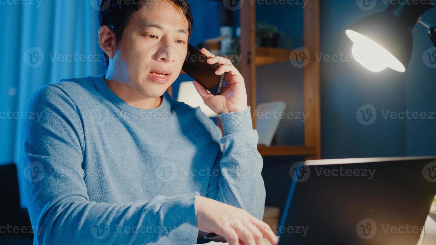 junge asiatische geschäftsleute verwenden Smartphone-Anruf-Agenda-Zuordnungspapiere mit Kollegen Blick auf Laptop-Computer im Wohnzimmer zu Hause Überstunden in der Nacht, Arbeit von zu Hause aus Corona-Pandemie-Konzept. foto
