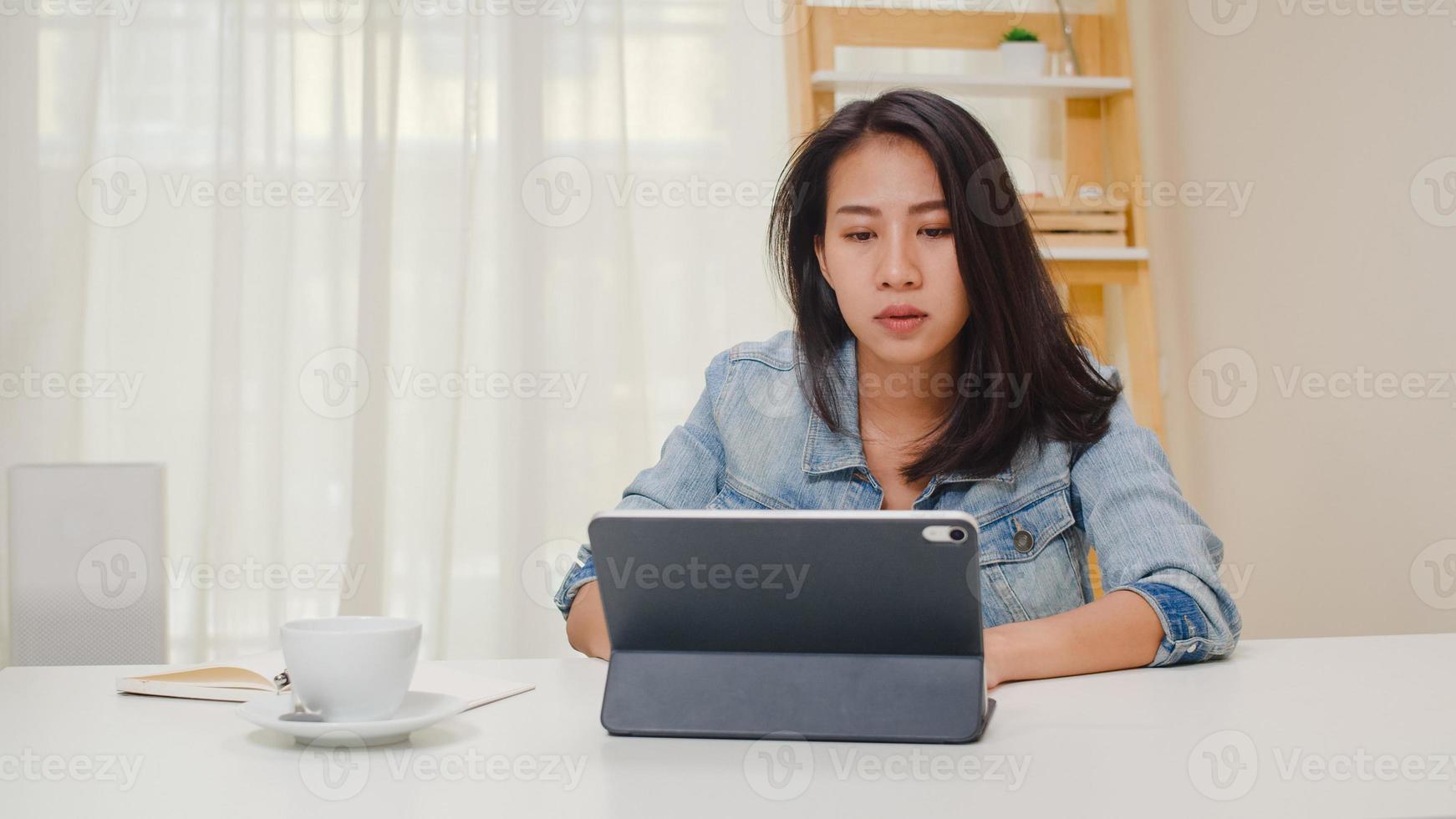 frustrierte junge asiatische Dame, die ein Problem mit dem nicht funktionierenden Tablet-Computer hat, der auf dem Schreibtisch sitzt. Freiberufliche Smart Business Women Casual Wear mit Tablet am Arbeitsplatz im Wohnzimmer im Home Office. foto