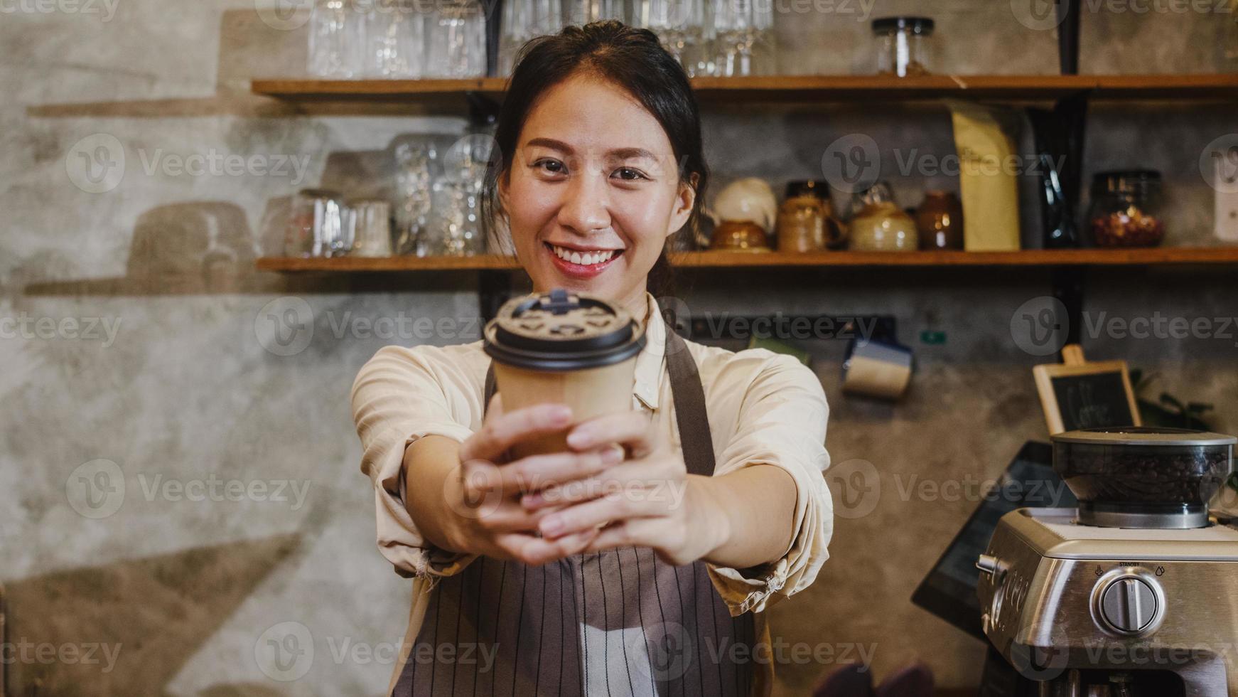 Porträt junge asiatische Dame Barista Kellnerin mit Kaffeetasse glücklich im städtischen Café. Asien Kleinunternehmer Mädchen in Schürze entspannen zahniges Lächeln mit Blick auf den Kamerastand an der Theke im Café. foto