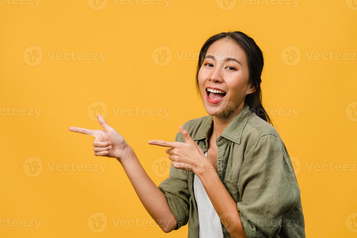 Porträt einer jungen asiatischen Dame, die mit fröhlichem Ausdruck lächelt, zeigt etwas Erstaunliches an leeren Stellen in legerem Tuch und blickt auf die Kamera einzeln auf gelbem Hintergrund. Gesichtsausdruck Konzept. foto