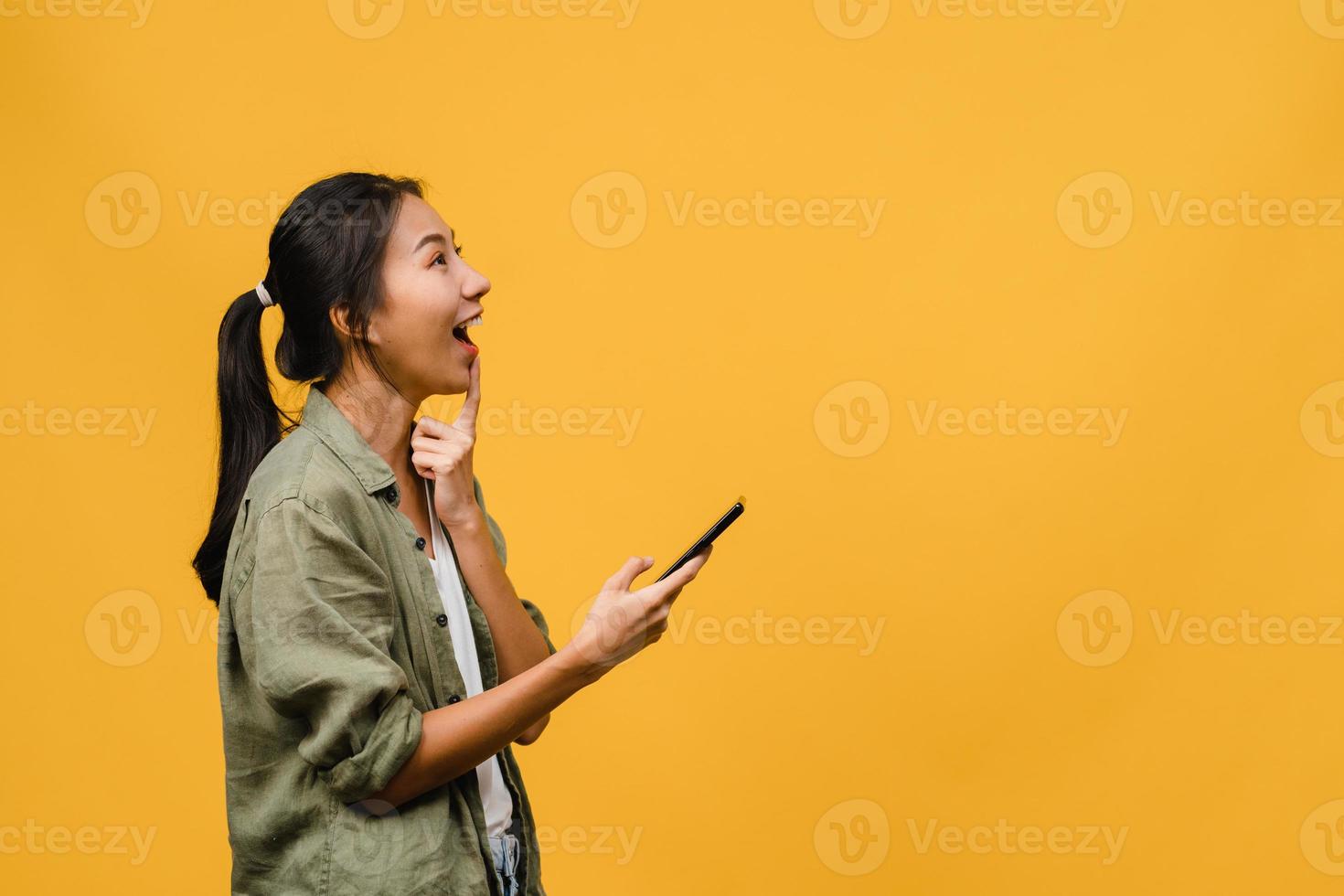 junge asiatische dame, die telefon mit positivem ausdruck verwendet, breit lächelt, in lässiger kleidung gekleidet fühlt sich glücklich und steht einzeln auf gelbem hintergrund. glückliche entzückende frohe frau freut sich über erfolg. foto