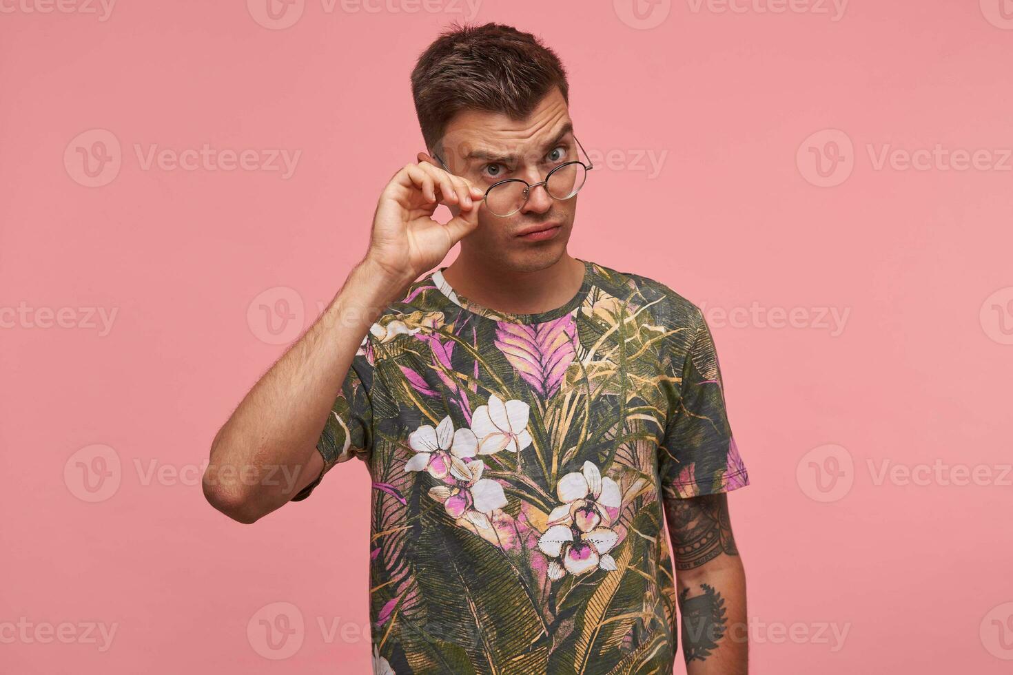 attraktiv jung Kerl nehmen aus Brillen und suchen von unter Stirn beim Kamera mit ernst Ausdruck, posieren Über Rosa Hintergrund foto