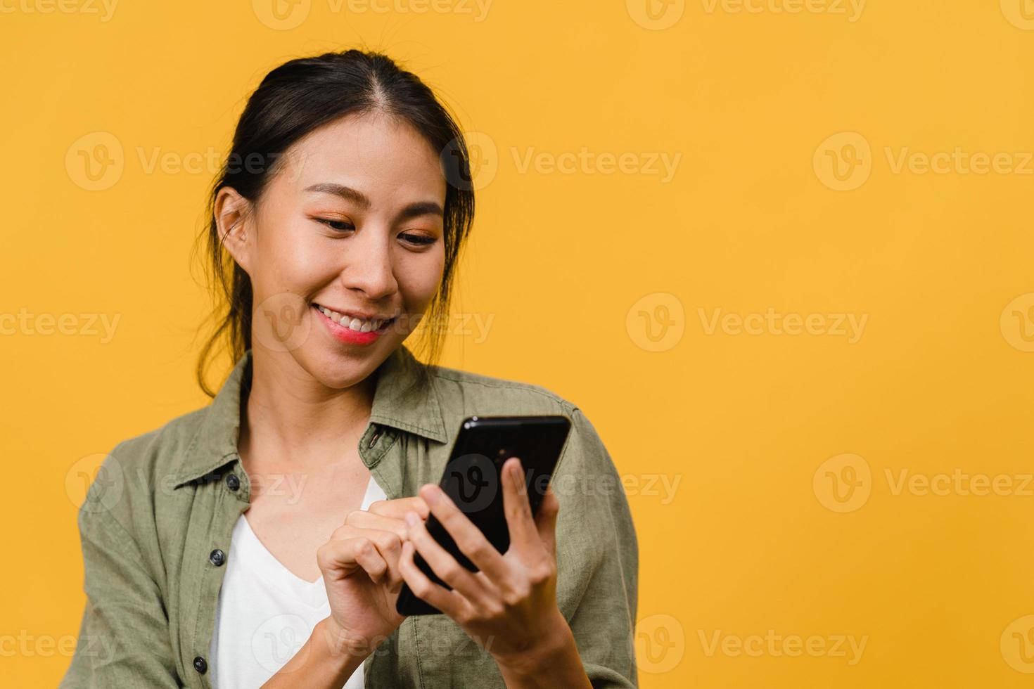 junge asiatische dame, die telefon mit positivem ausdruck verwendet, breit lächelt, in lässiger kleidung gekleidet fühlt sich glücklich und steht einzeln auf gelbem hintergrund. glückliche entzückende frohe frau freut sich über erfolg. foto