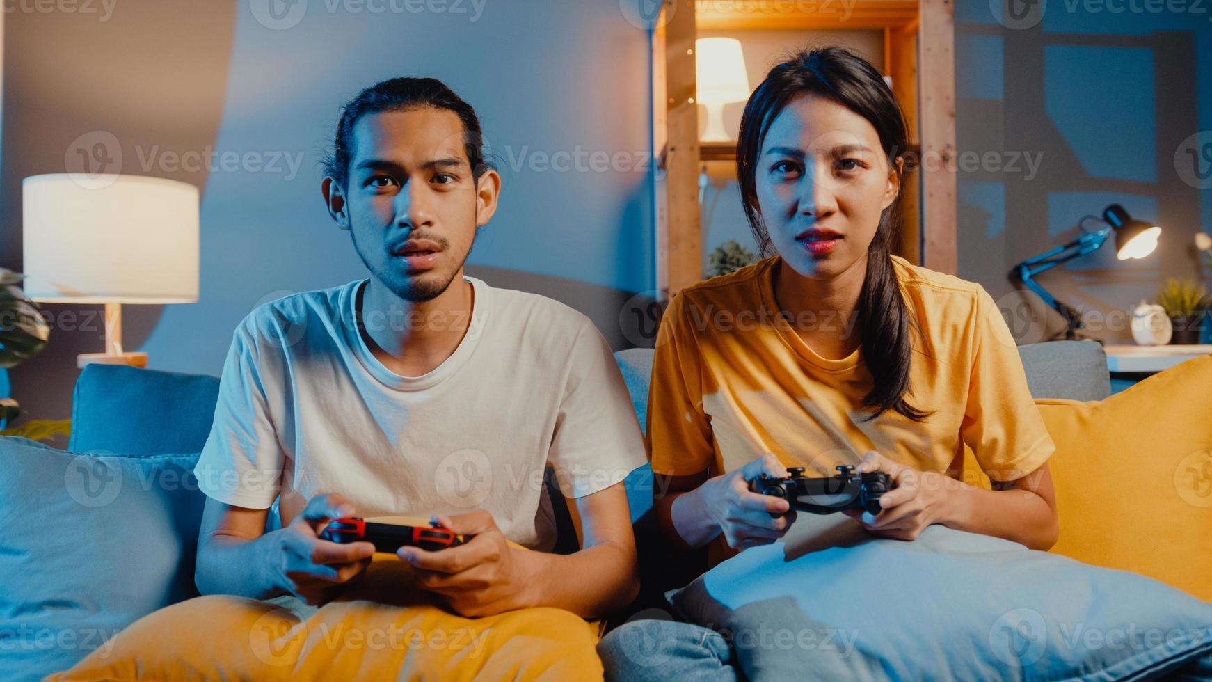 glückliches asiatisches junges Paar Mann und Frau sitzen auf der Couch mit Joystick-Controller spielen Videospiele verbringen lustige Zeit zusammen im Wohnzimmer in der Nacht. asiatisches Ehepaar Familienleben, bleiben Sie zu Hause Konzept. foto