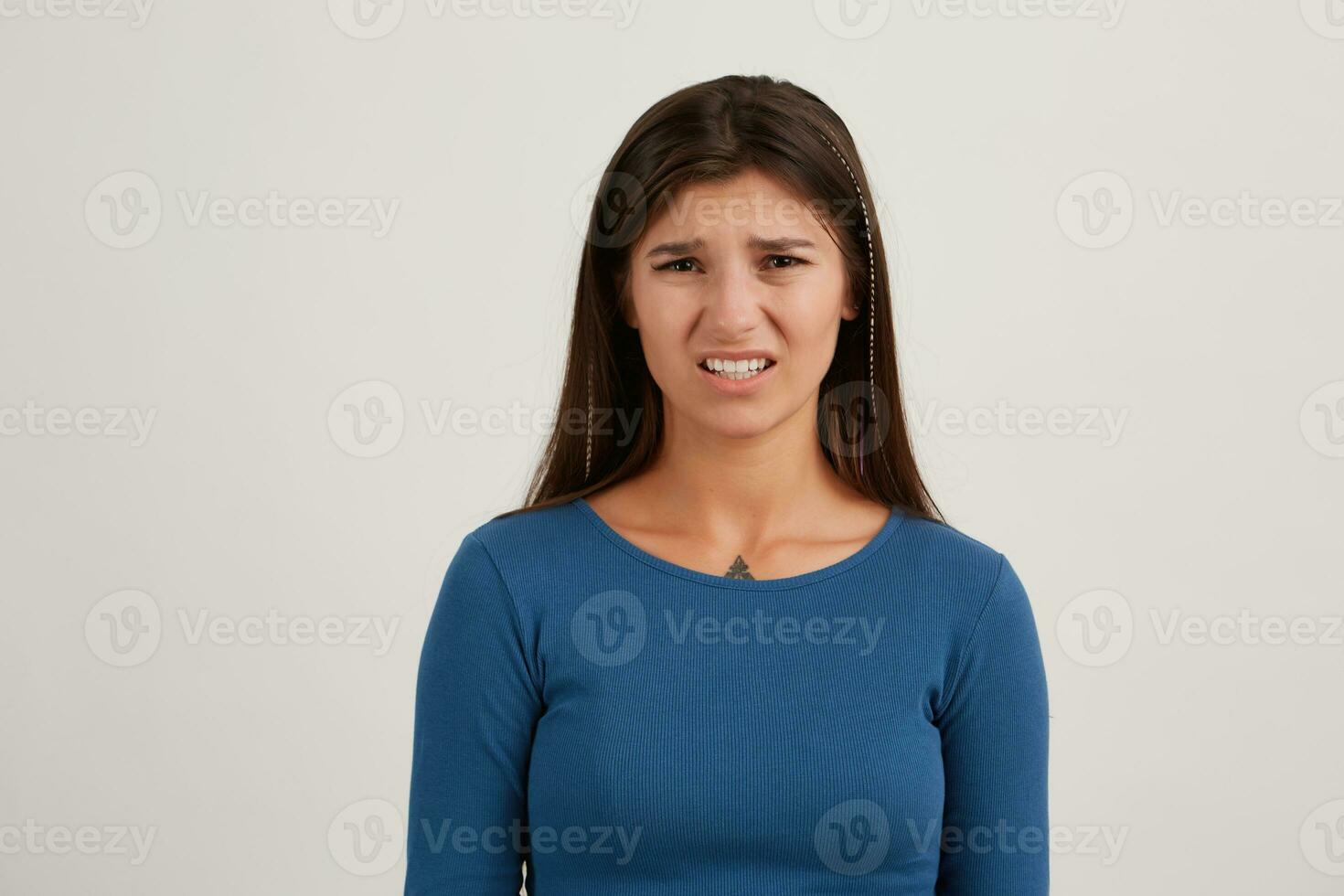 Porträt von unzufrieden, unzufrieden Mädchen mit dunkel lange Haar. tragen Blau Jumper. hat Tätowierung. Emotion Konzept. Aufpassen und runzelt die Stirn beim das Kamera isoliert Über Weiß Hintergrund foto