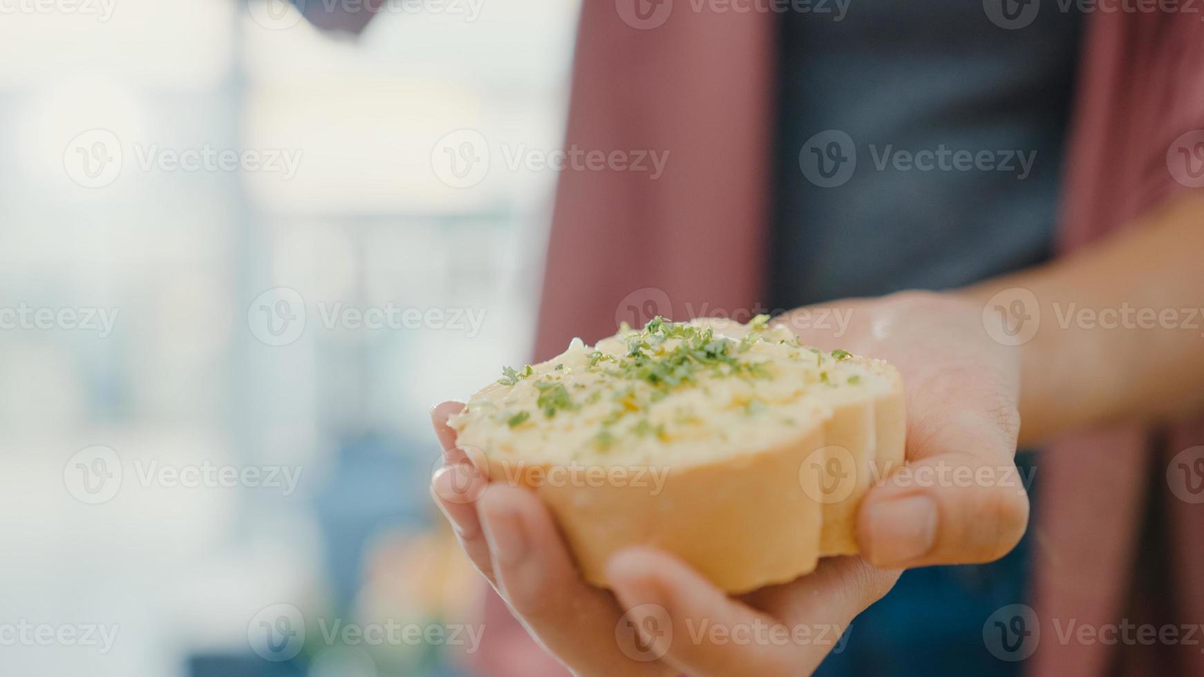 Hand der jungen asiatischen Köchin verteilt Knoblauchbutter auf rustikalem Roggenbrot mit Metallmesser auf Holzbrett auf Küchentisch im Haus. frische hausgemachte Brotproduktion, gesunde Ernährung und traditionelle Bäckerei. foto