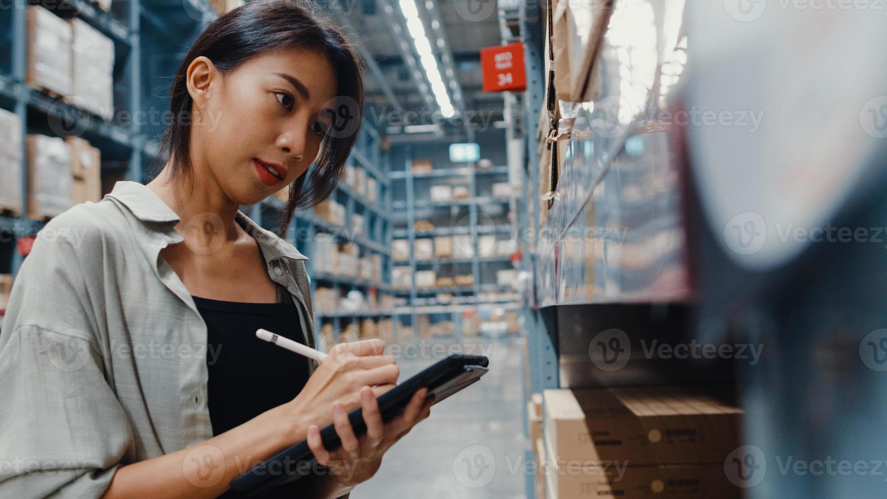 Attraktive junge Geschäftsfrau in Asien, die nach Waren sucht, indem sie digitale Tablets verwendet, um die Lagerbestände im Einzelhandels-Einkaufszentrum zu überprüfen. Distribution, Logistik, versandfertige Pakete. foto