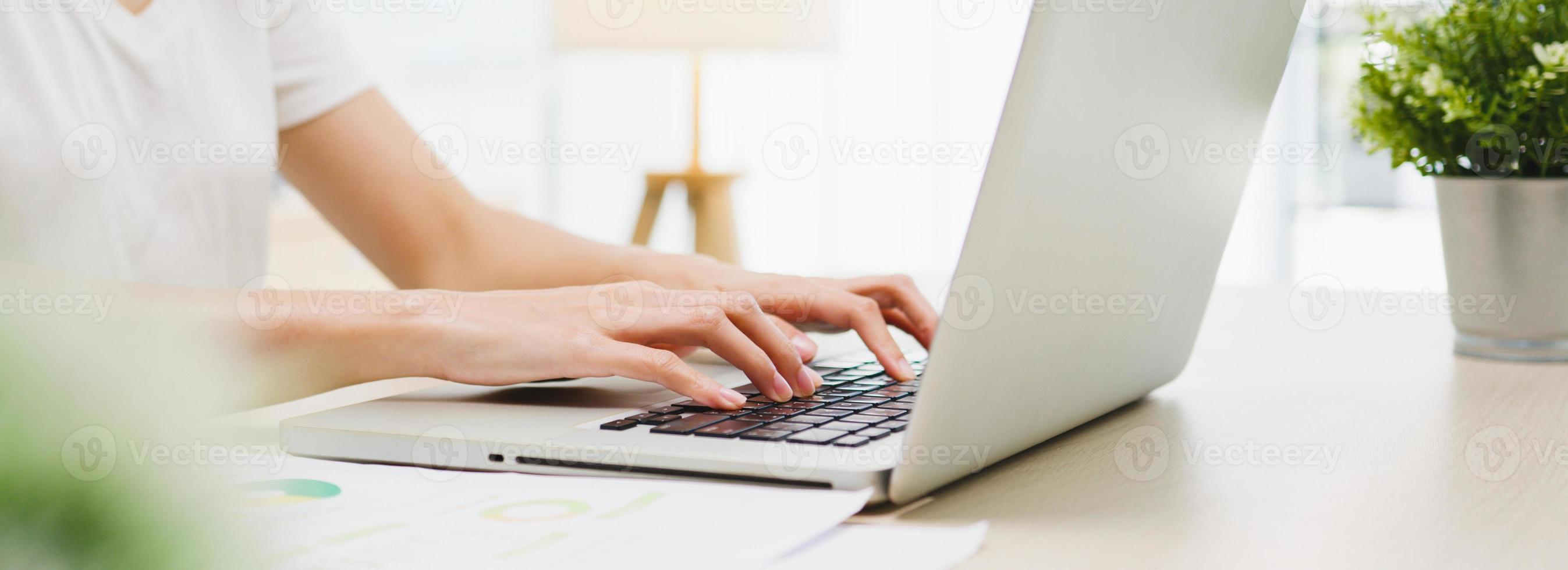 Freiberufliche asiatische Geschäftsfrau Freizeitkleidung mit Laptop im Wohnzimmer zu Hause arbeiten. aus der Ferne, soziale Distanzierung, Quarantäne zur Vorbeugung von Coronaviren. Panorama-Banner-Hintergrund mit Kopienraum. foto