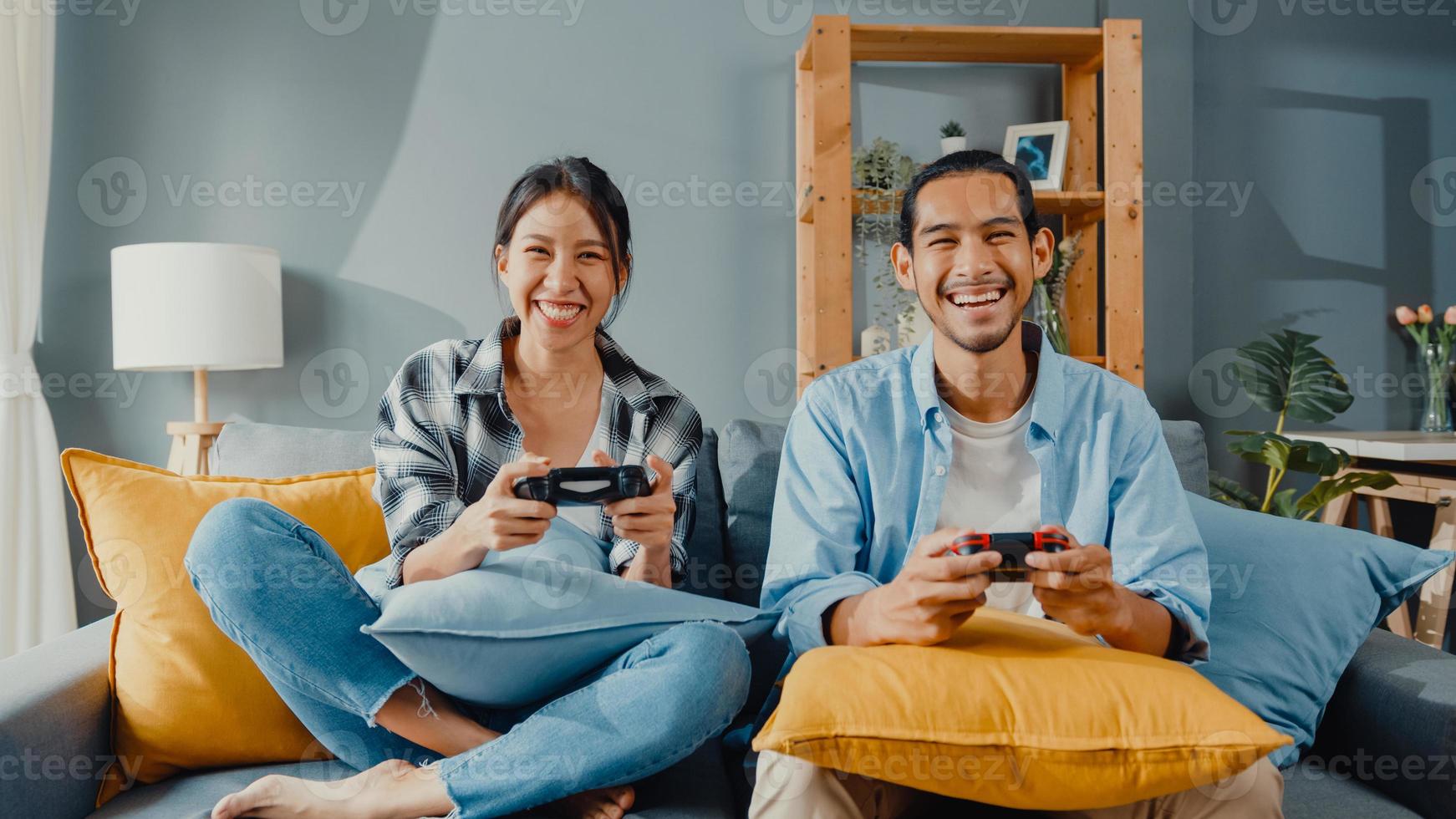 glückliches asiatisches junges paar mann und frau sitzen auf der couch und verwenden einen Joystick-Controller, um ein Videospiel zu spielen, verbringen lustige Zeit zusammen im Wohnzimmer. asiatisches Ehepaar Familienleben, Paar bleibt zu Hause Konzept. foto