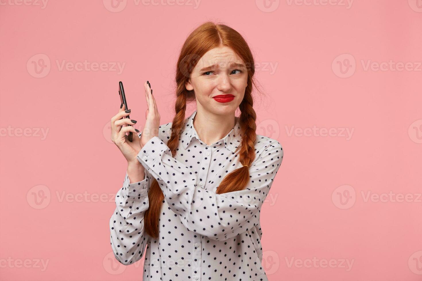 Mädchen mit rot Zöpfe hält das Telefon beim ein Entfernung aus, Zäune aus mit Hand von Es, runzelt die Stirn beim das Tatsache Das das andere Person Geschrei, schwört, ein unangenehm Telefon Gespräch, ein Streit. foto