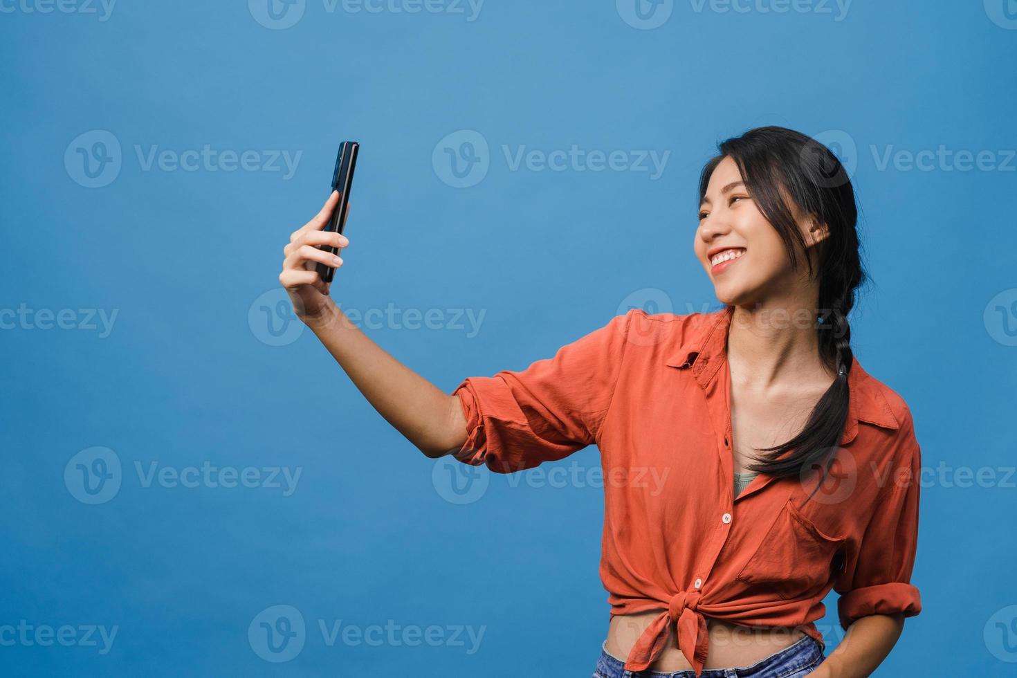 Lächelnde entzückende asiatische Frau, die Selfie-Foto auf Smartphone mit positivem Ausdruck in Freizeitkleidung macht und auf blauem Hintergrund steht. glückliche entzückende frohe frau freut sich über erfolg. foto