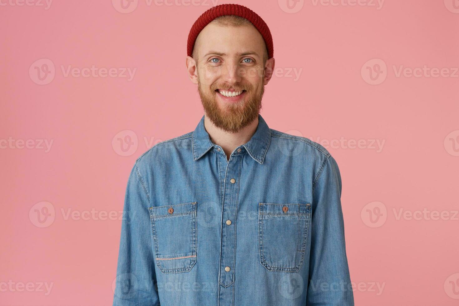 froh froh Kerl im rot Hut mit rot dick Bart lächelnd glücklich zeigen Weiß gesund Zähne, trägt modisch Denim Shirt, isoliert auf Rosa Hintergrund foto