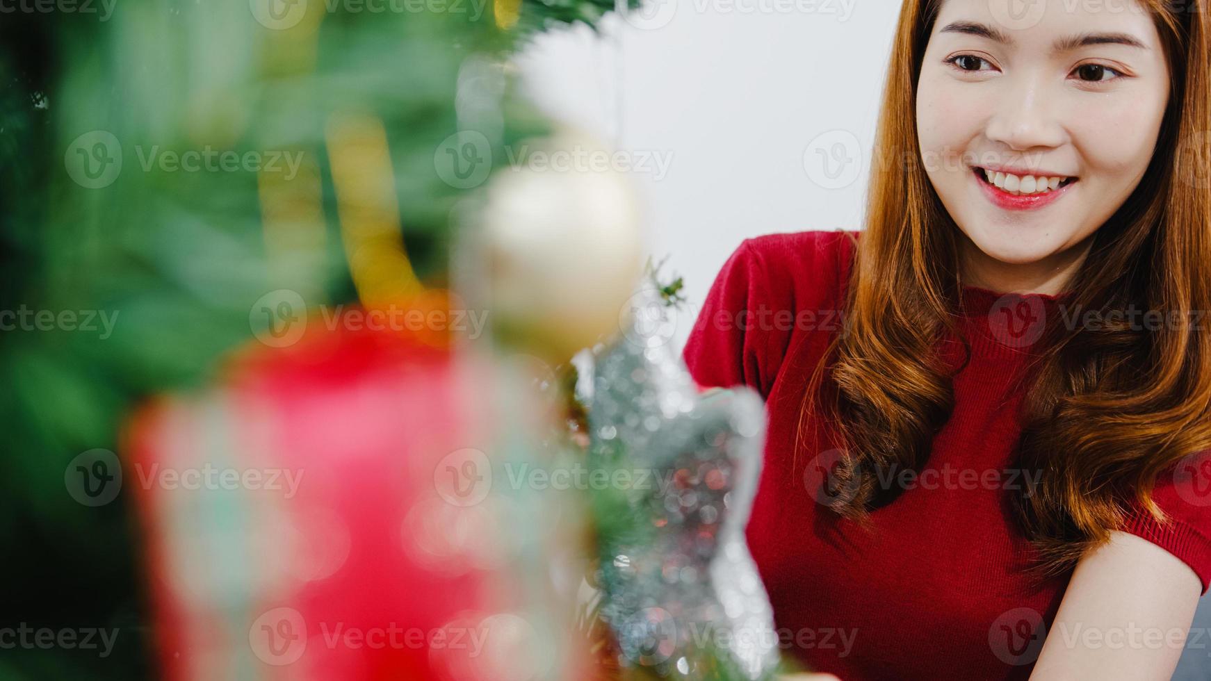 asiatische Frau mit Ornament am Weihnachtsbaum zu Weihnachten und Neujahrsfest im Wohnzimmer zu Hause dekoriert. Weihnachtsfeier Veranstaltungsvorbereitung oder Winterferien Festival Indoor-Party-Konzept. foto