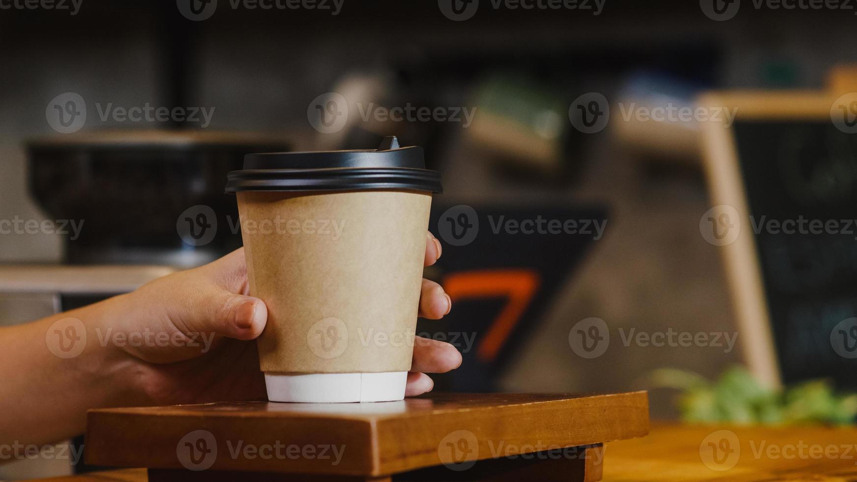 junge asiatische Barista, die den Verbraucher hinter der Theke im Café-Restaurant zum Mitnehmen heißer Kaffee-Pappbecher serviert. Inhaber kleines Unternehmen, Essen und Trinken, Service-Geist-Konzept. foto