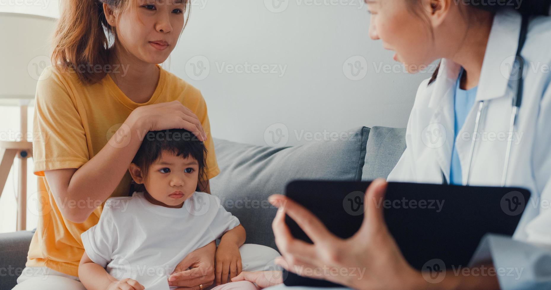 Junge asiatische Kinderärztin und kleine Mädchenpatientin mit digitaler Tablette, die gute Gesundheitstestnachrichten mit glücklicher Mutter teilt, sitzt auf der Couch im Haus. Krankenversicherung, besuchen Sie den Patienten zu Hause Konzept. foto