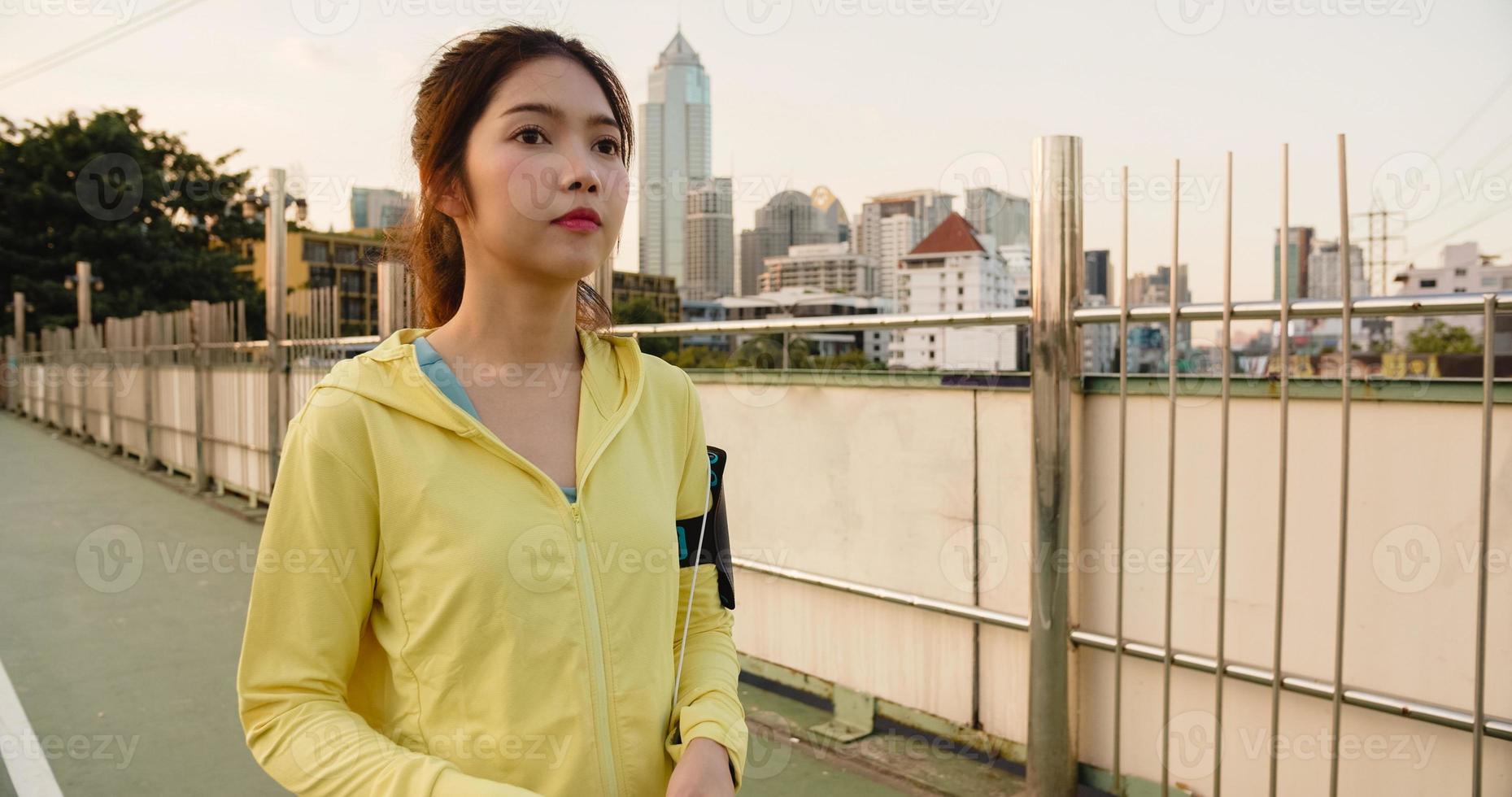 Schöne junge asiatische Sportlerin trainiert mit dem Smartphone, um Musik beim Laufen in der städtischen Umgebung zu hören. koreanisches jugendlich Mädchen, das am frühen Morgen Sportkleidung auf der Gehwegbrücke trägt. foto