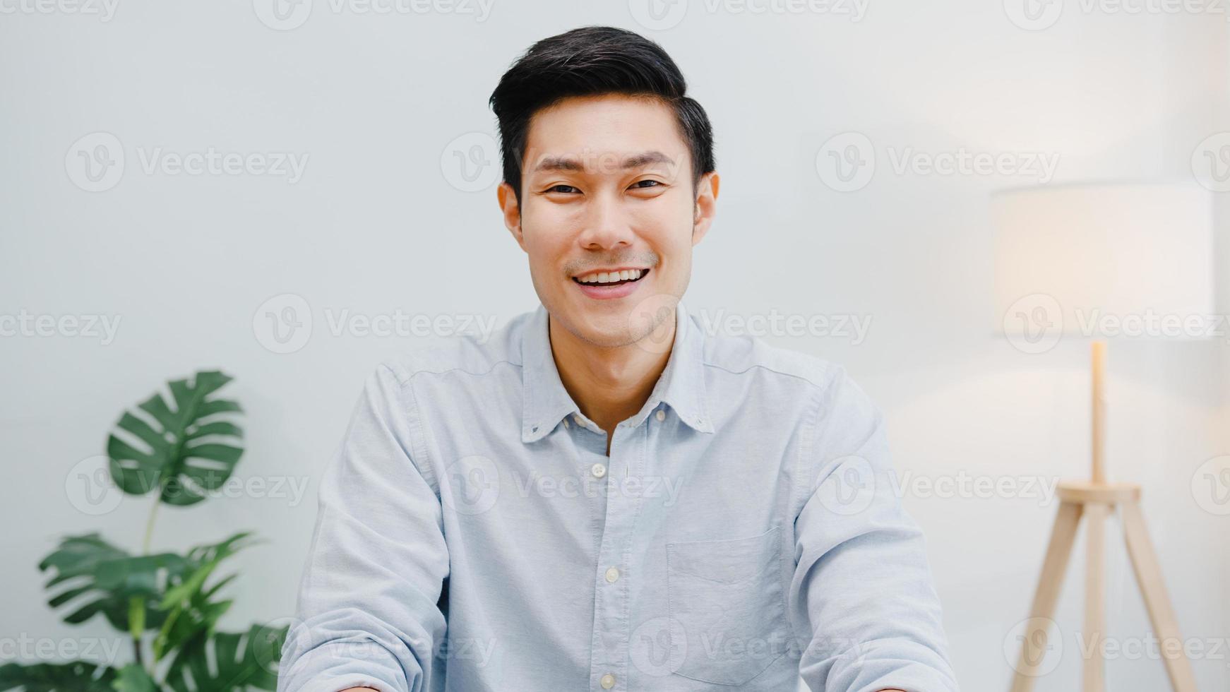 Porträt eines erfolgreichen, gutaussehenden Geschäftsmannes, Smart Casual Wear, der die Kamera anschaut und lächelt, glücklich am modernen Büroarbeitsplatz. junger asiatischer kerl spricht mit kollege in videoanrufbesprechung zu hause. foto
