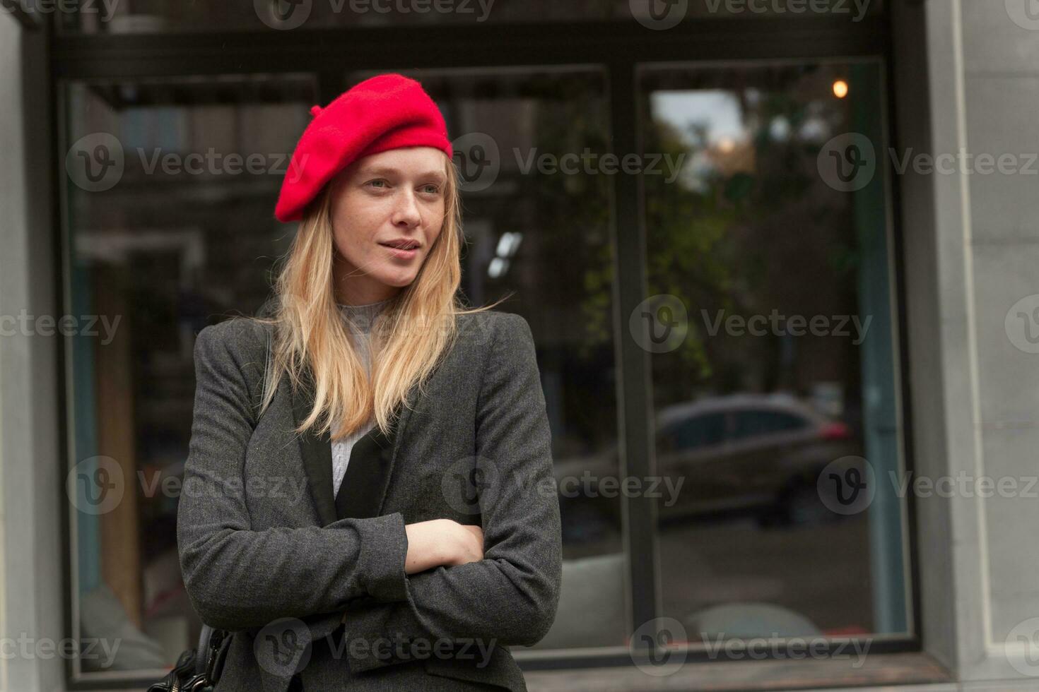 Porträt von charmant jung blond lange behaart Frau im elegant Kleider behalten ihr Hände gekreuzt und suchen beiseite nachdenklich während Stehen Über Cafe Außen foto