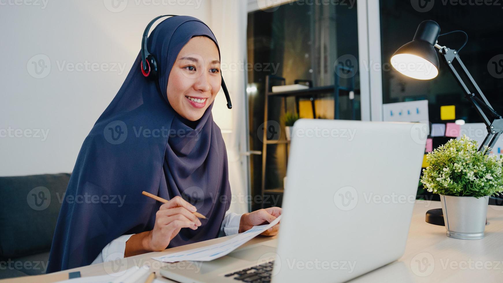 asien muslimische dame tragen kopfhörer webinar hören online kurs kommunizieren per konferenz-videoanruf in der nacht im heimbüro. Fernarbeit von zu Hause aus, soziale Distanz, Quarantäne für Corona-Virus. foto