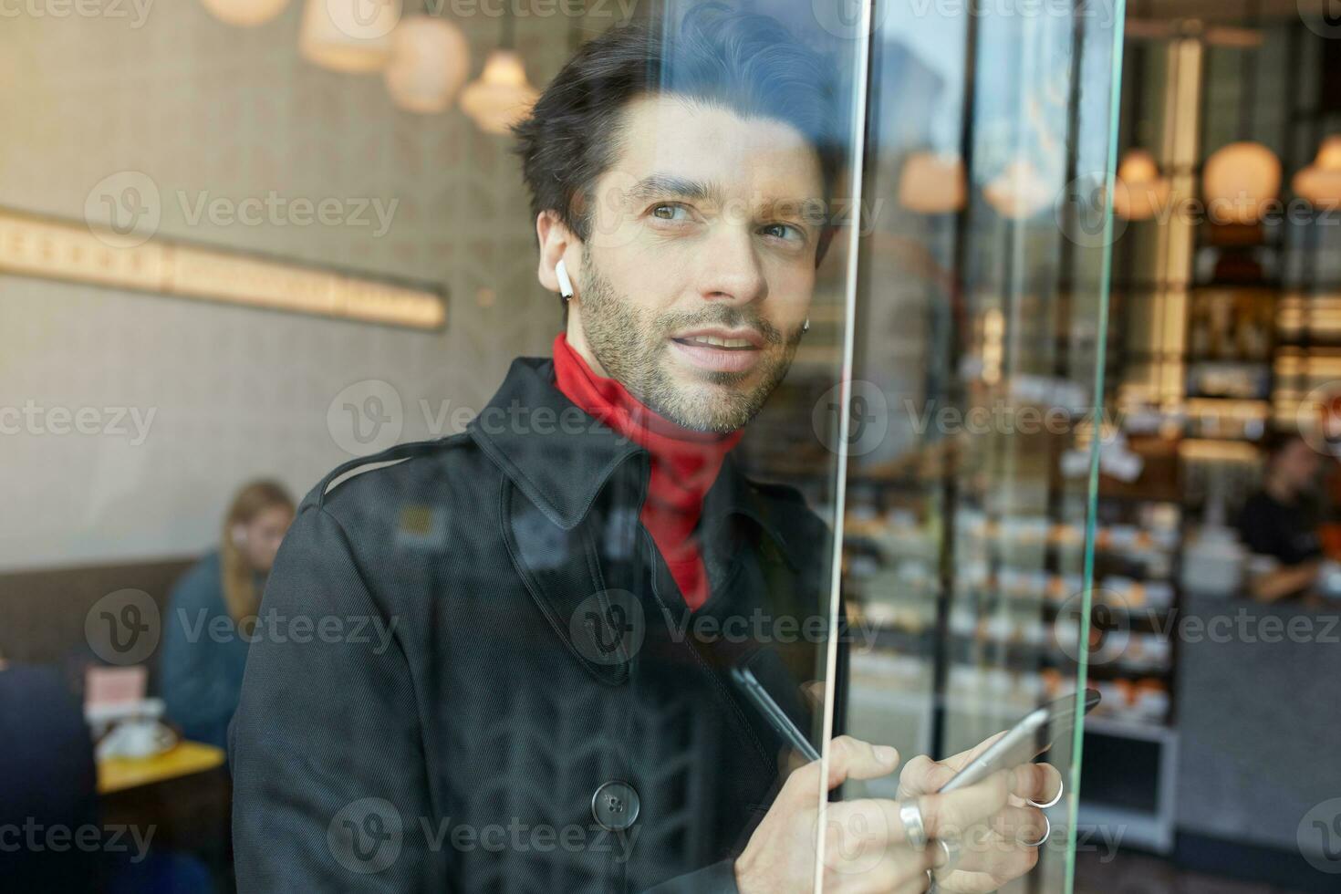 Porträt von nachdenklich jung ziemlich unrasiert Brünette Kerl gekleidet im elegant Kleider suchen nachdenklich aus von Fenster während Hören zu Musik- mit Kopfhörer foto